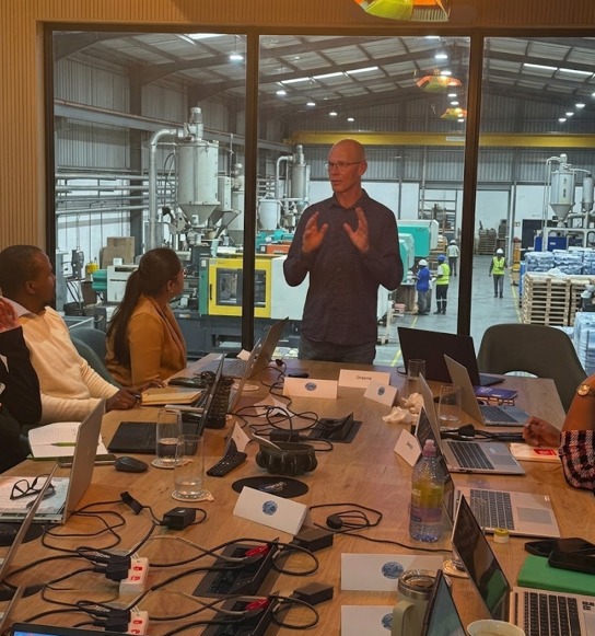 Graeme Pitt facilitating a Generative AI Productivity Workshop in a boardroom overlooking the factory floor, with delegates working on laptops